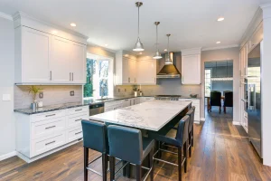 Contemporary kitchen featuring a large quartz countertop island, white cabinetry, and stainless steel appliances in a bright setting.