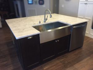 Stainless steel apron farm sink with single bowl and modern faucet on quartz countertop in a kitchen setting.