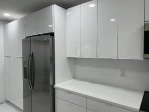 Sleek white kitchen cabinets with a stainless steel refrigerator and quartz countertop, showcasing contemporary kitchen design.
